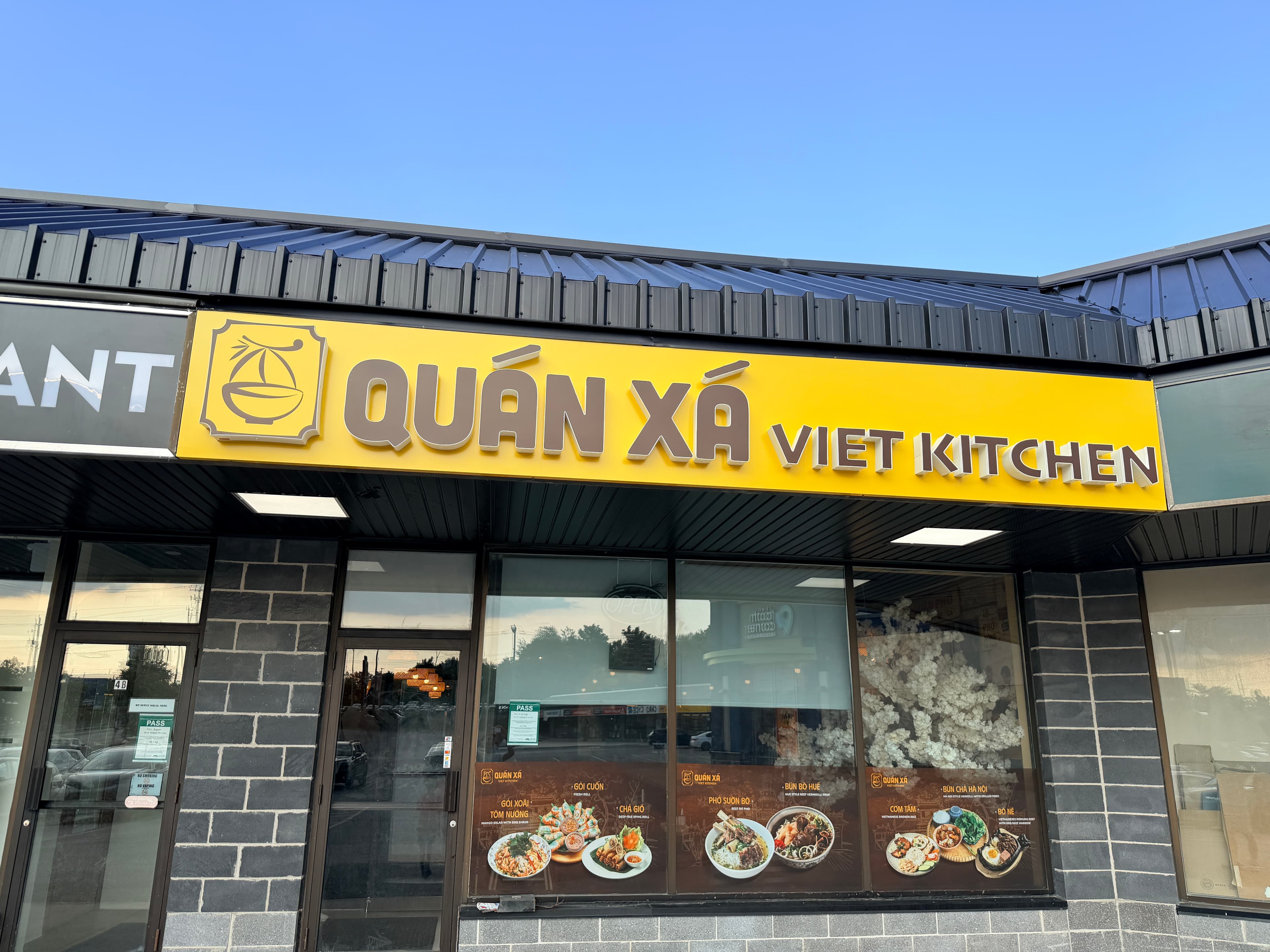 Yellow sign for Quán Xá Viet Kitchen restaurant above a storefront with food photos.